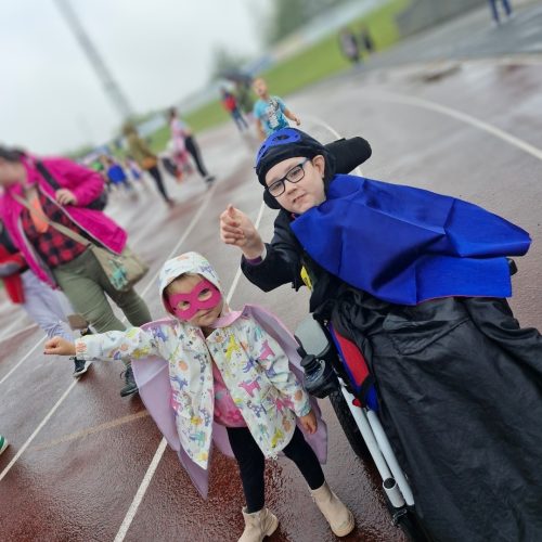 Two young children wearing superhero masks and capes on a race track